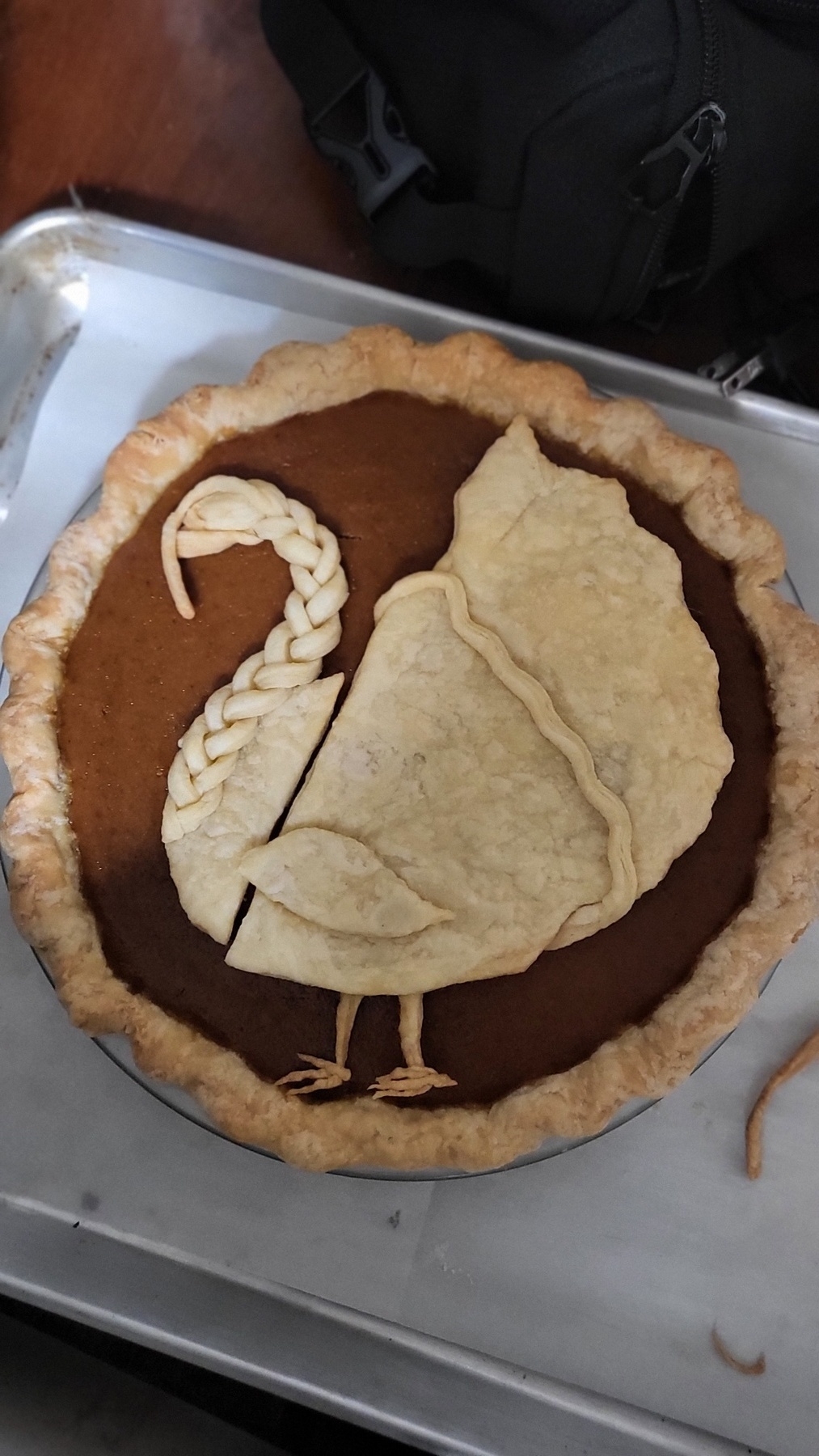 A turkey shaped set of dough pieces on a pie. The neck is braided dough, there's a little wing, and two thin turkey feet. 